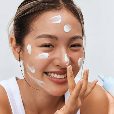 Mulher a aplicar creme no rosto durante a rotina de skincare, num cenário clean e luminoso.